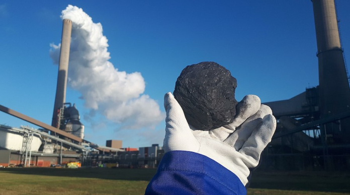 Worker-holding-up-a-piece-of-coal-in-front-of-a-coal-firing-power-plant-in-the-Netherlands