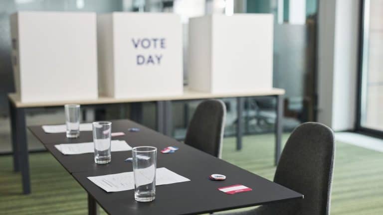A prepared voting station with tables, chairs, and privacy booths in a conference room.